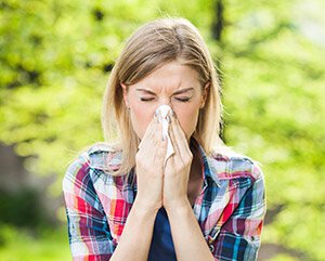 woman with allergies blowing nose